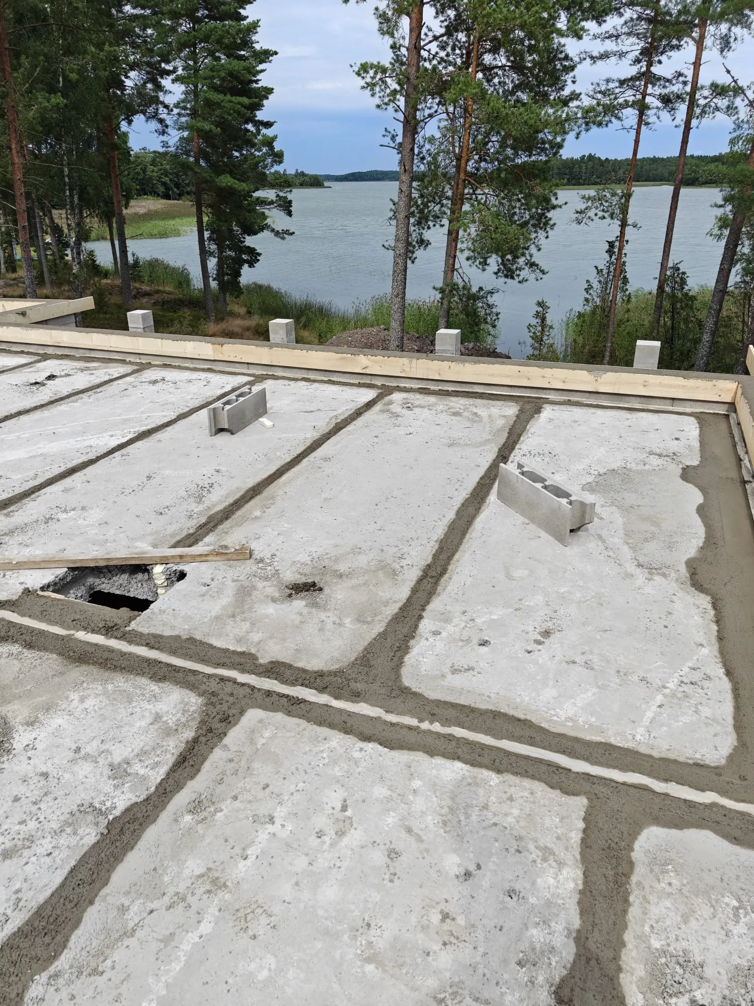 Rakenteilla olevan betonilaatan saumoja täytetään laastilla, taustalla näkyy järvimaisema mäntyineen.