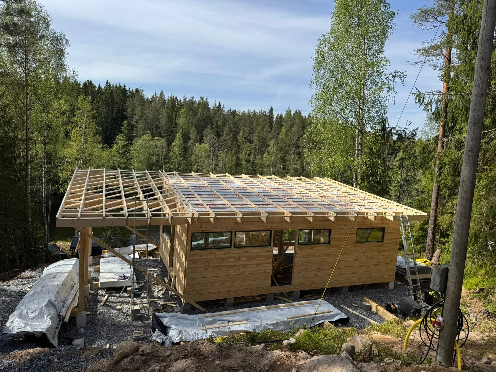 Puinen talo on rakenteilla metsäisessä ympäristössä, ja sen kattorakenne on jo pystytetty.