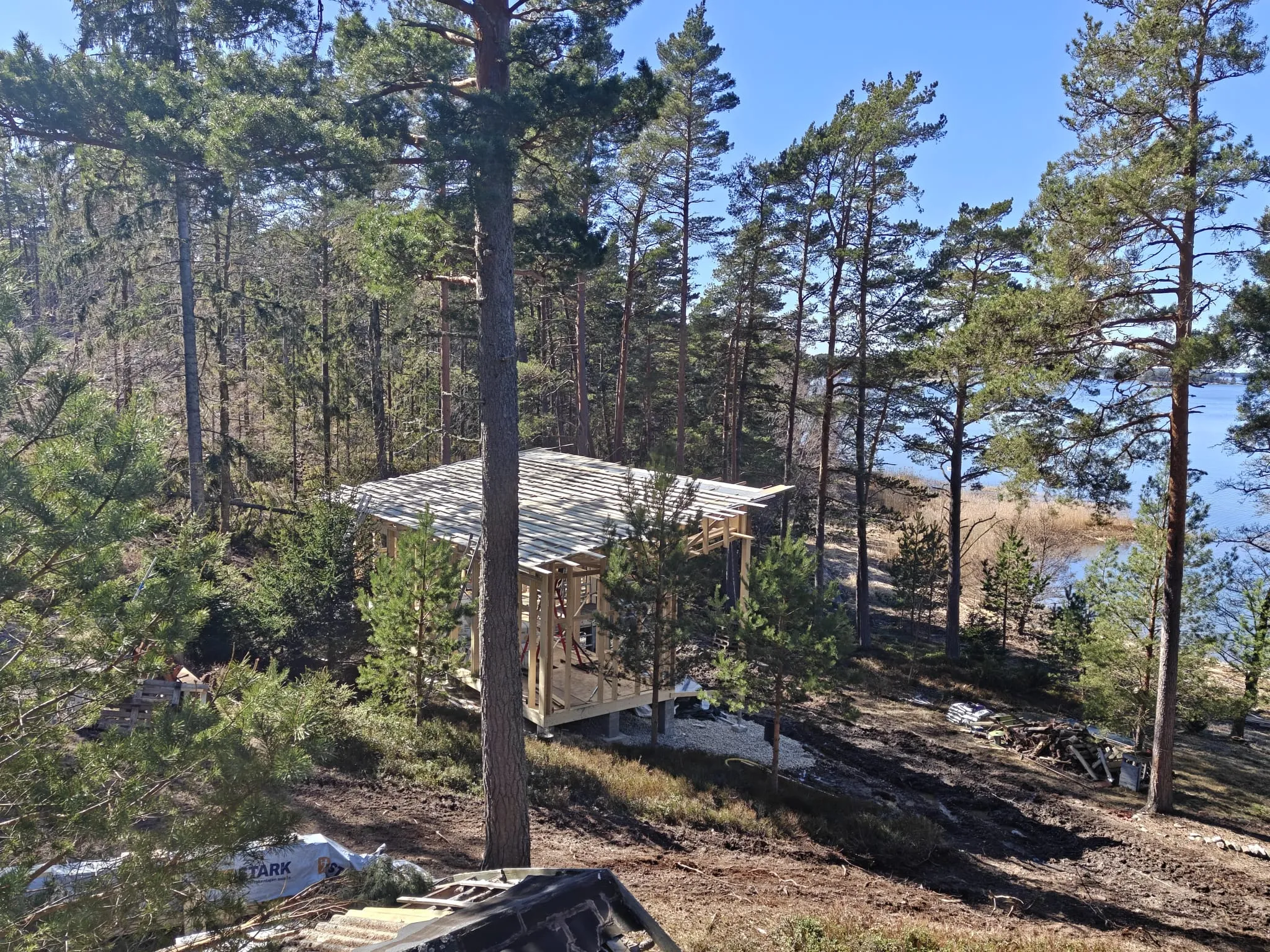 Mäntymetsäisellä tontilla järven rannalla on puurunkoinen rakennus rakentamisen alkuvaiheessa.