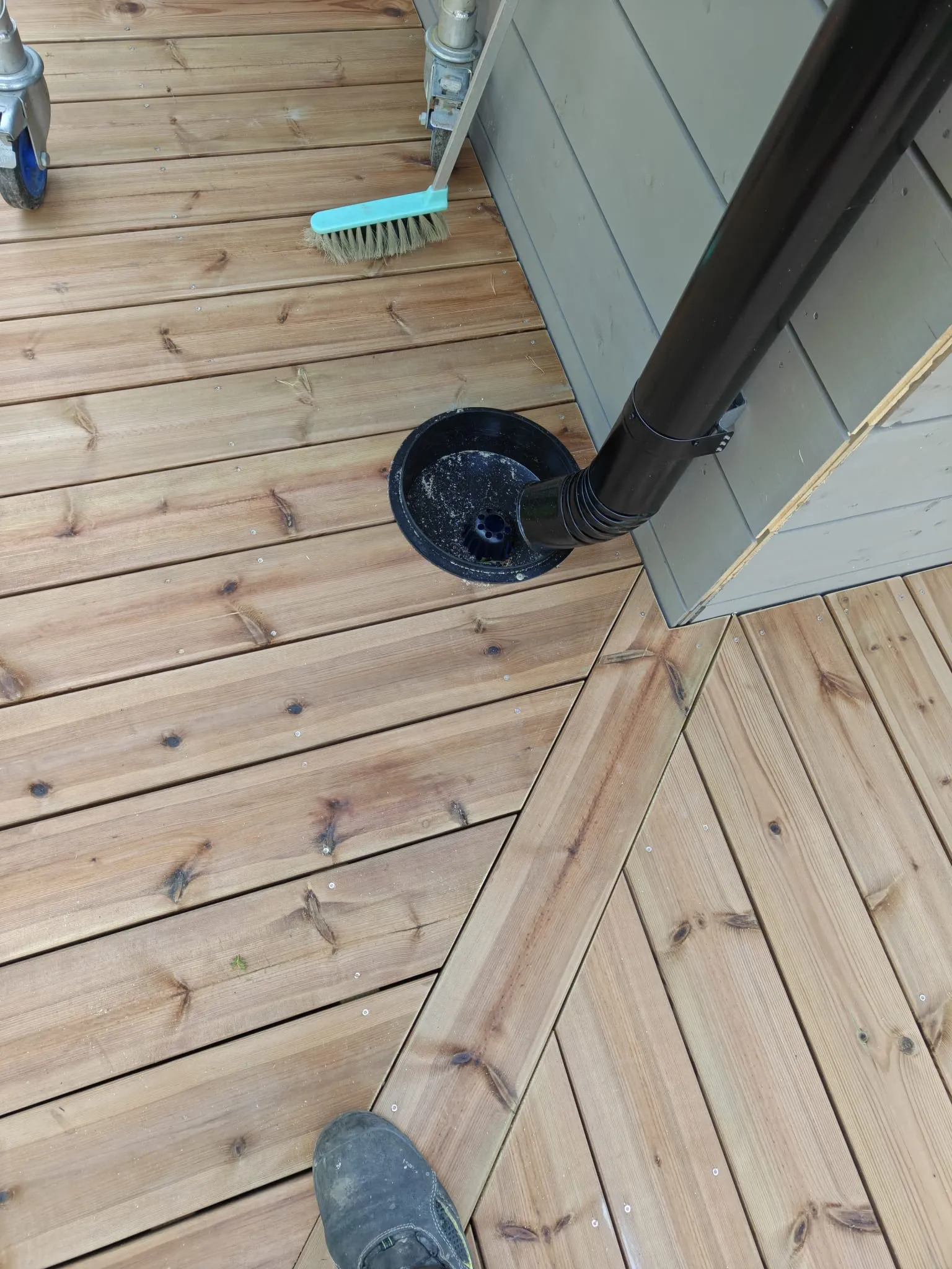 Puinen terassi ja musta syöksytorvi sadevesikaivolla rakennuksen seinän vieressä.